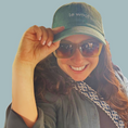 Load image into Gallery viewer, Picture of Le Woof Founder, Hila Raz Harris, wearing Le Woof Baseball Cap and smiling on a light green, sage toned background
